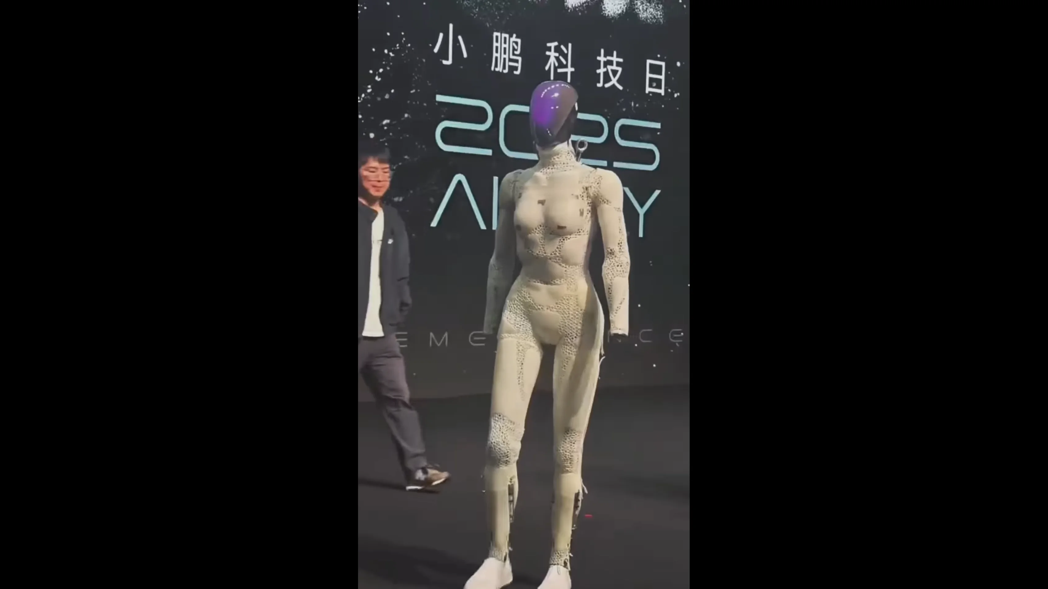 A female-styled Xpeng Iron robot walking across a stage without its outer white clothing or hands. The robot’s body is covered in a textured "bionic muscle" lattice structure that mimics human musculature. The arms end at the wrists, giving the figure an unfinished, eerie appearance.
