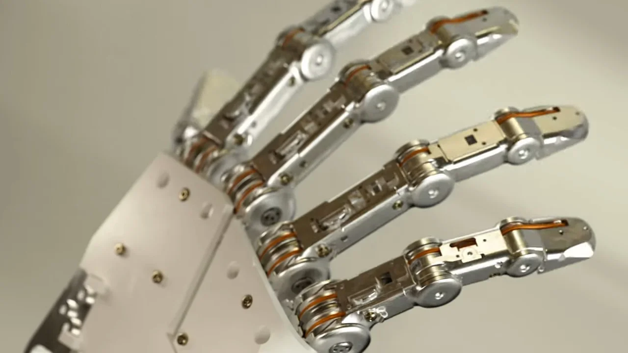 A high-detail close-up of a sleek, silver robotic hand showing four fingers with intricate internal joints and thin orange cables acting as tendons.