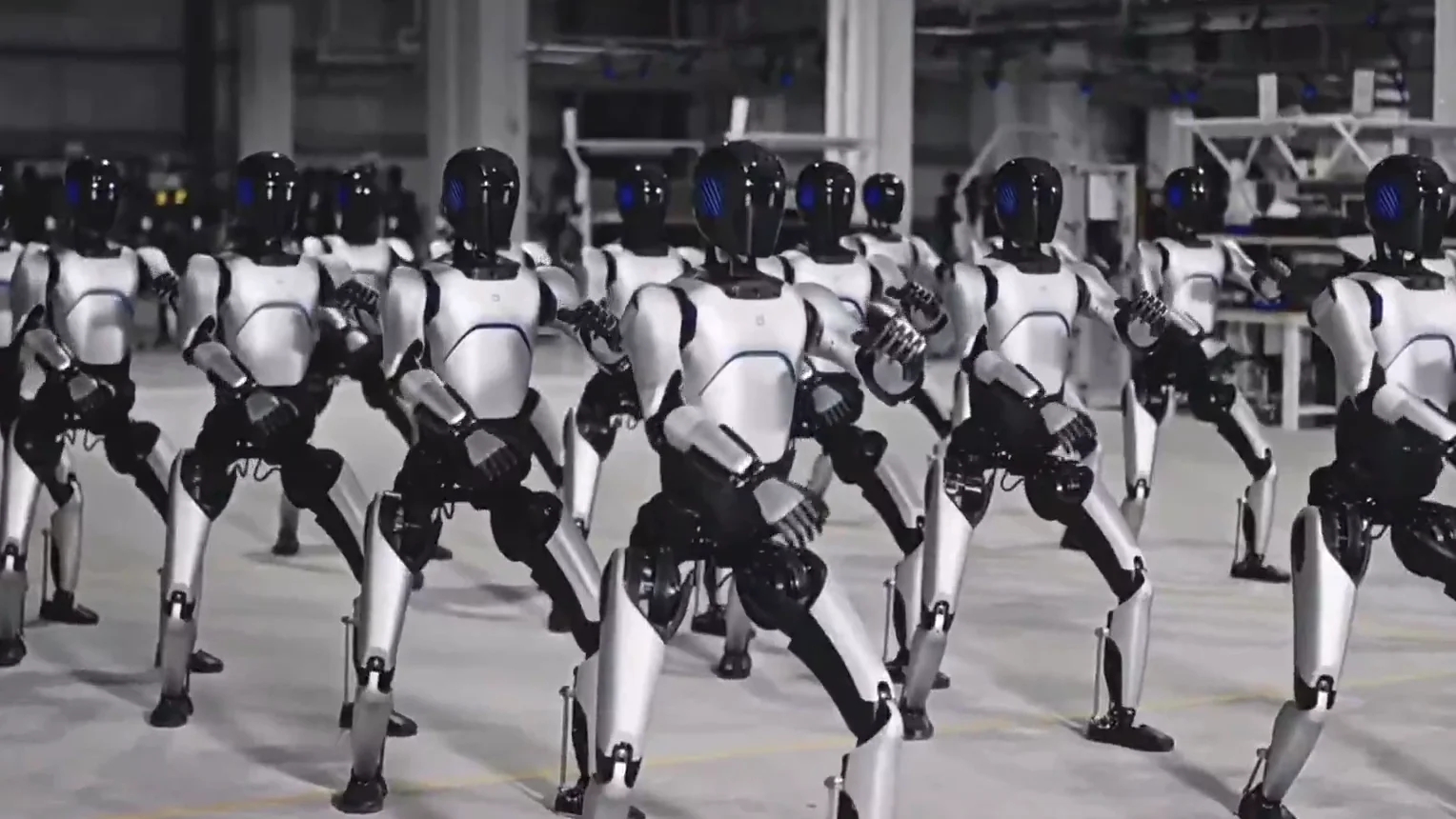 Rows of silver and black AgiBot humanoid robots standing in formation in a large industrial facility.