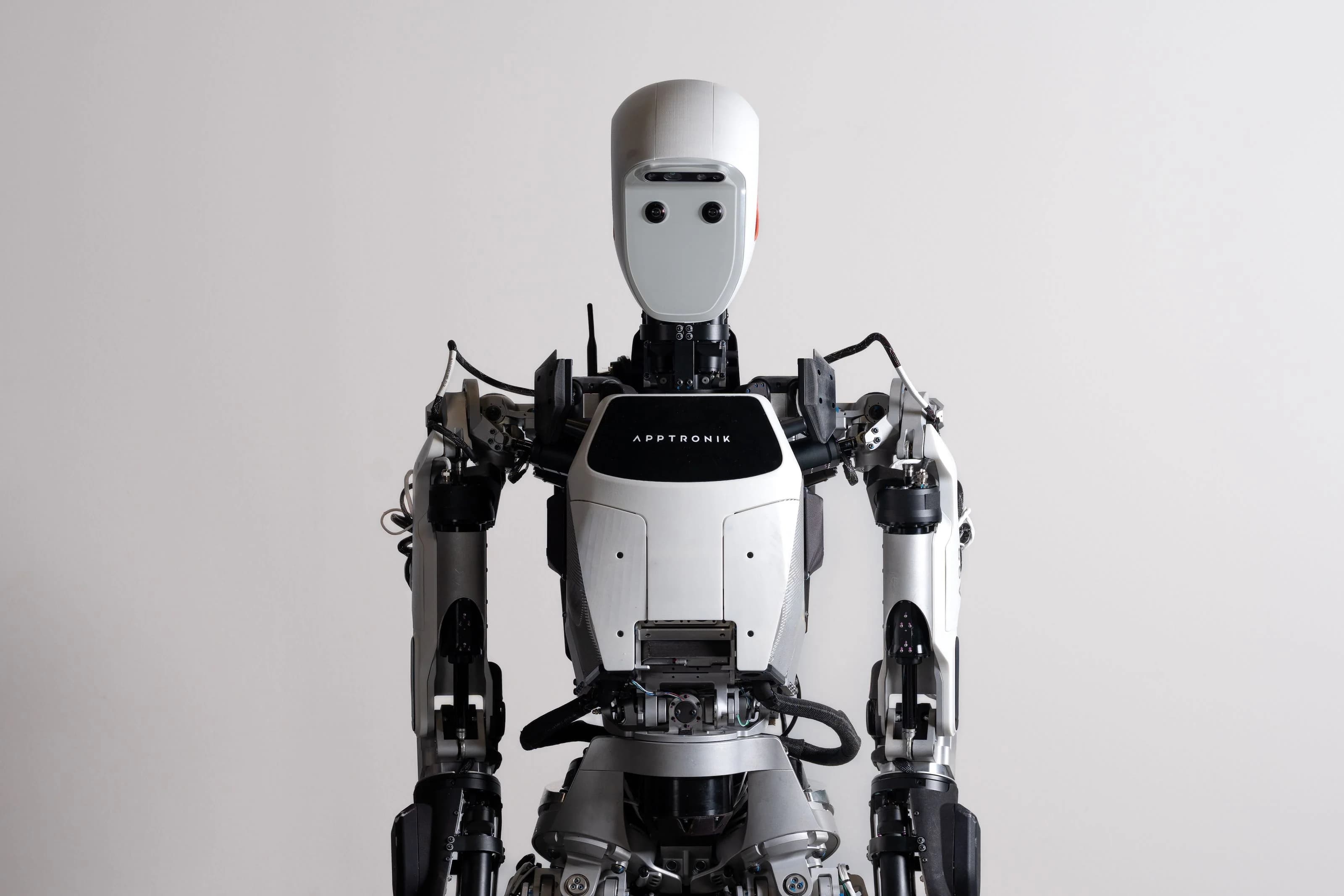A front-facing studio shot of the Apptronik Apollo robot from the waist up, showing its white chest plate with the company logo, mechanical arms, and sensor-equipped head.