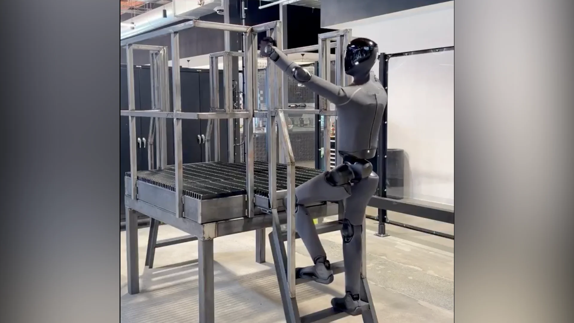 A side profile view of a dark grey Figure 03 humanoid robot with a glossy black faceplate climbing a short, custom metal ladder. The robot is reaching up with its right hand to grip the metal railing while stepping up onto a lower rung with its left foot inside an industrial laboratory environment.