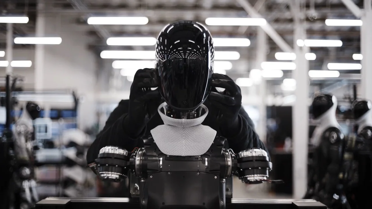A front-facing, ground-level perspective showing long rows of white Figure 03 robots standing on black bases, emphasizing the scale of the manufacturing output at the California facility.