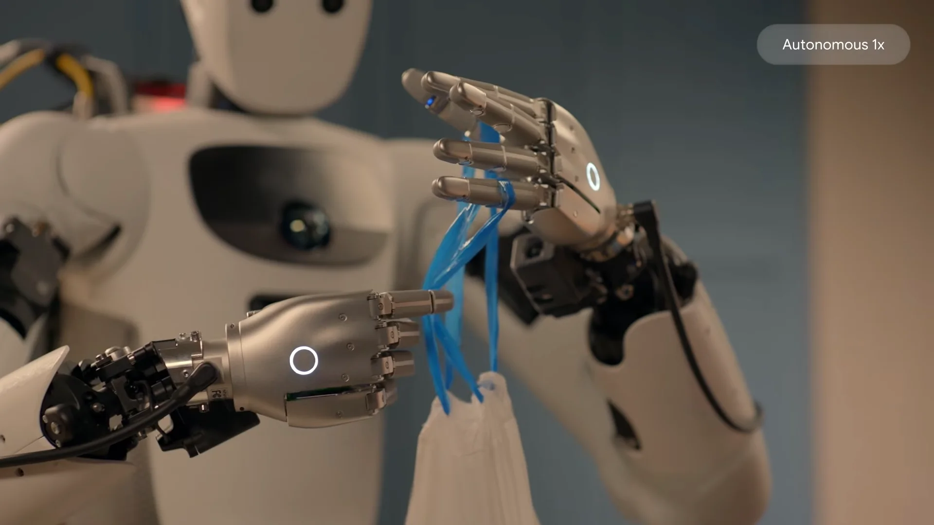 A close-up of a white humanoid robot utilizing metallic, five-fingered robotic hands to precisely manipulate and tie the thin blue plastic handles of a white bag. An overlay text reads 'Autonomous 1x'.
