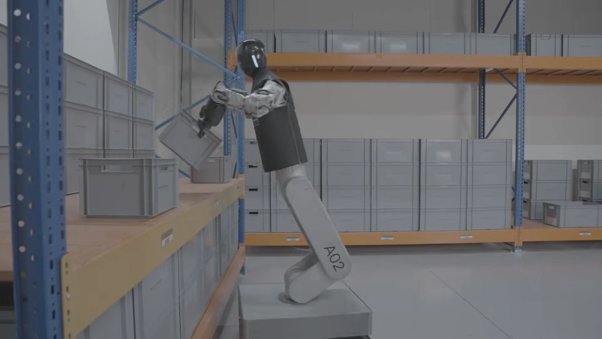 A side view of the wheeled HMND 01 Alpha robot, marked with 'A02' on its leg and wearing a black fabric 'uniform,' as it uses its mechanical arms to lift a grey KLT box from a wooden warehouse shelf.