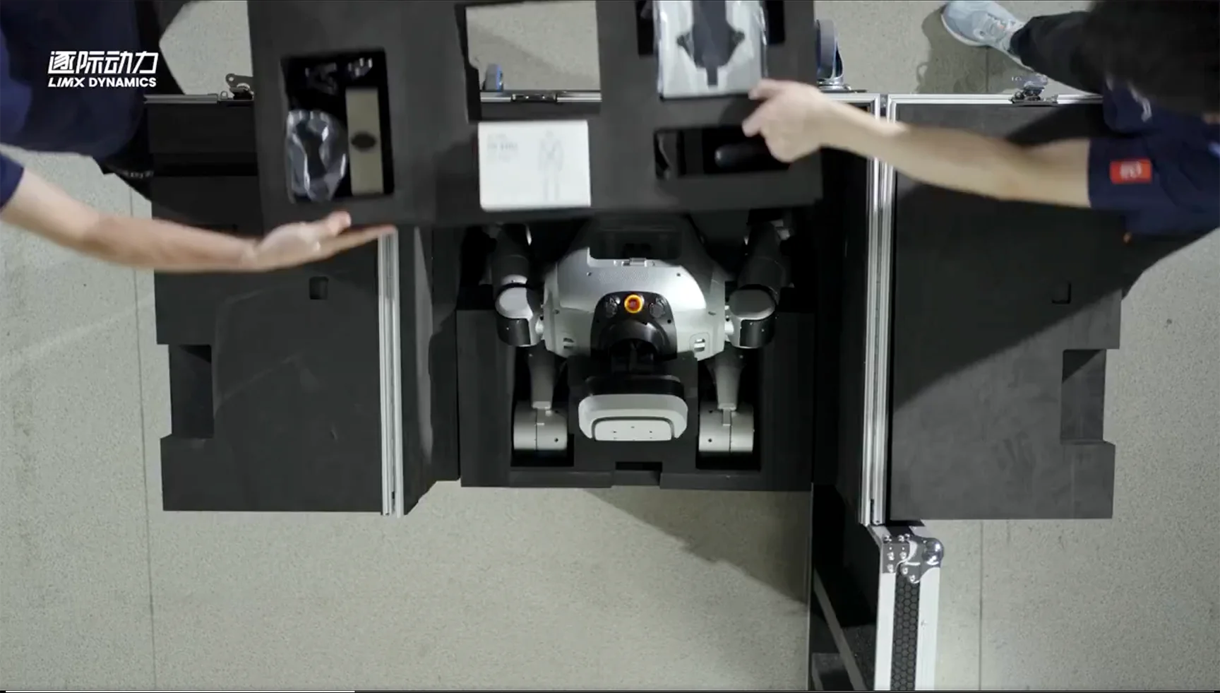 An overhead view showing two handlers opening a shipping case, revealing the LimX Dynamics Oli robot folded compactly inside custom foam padding.