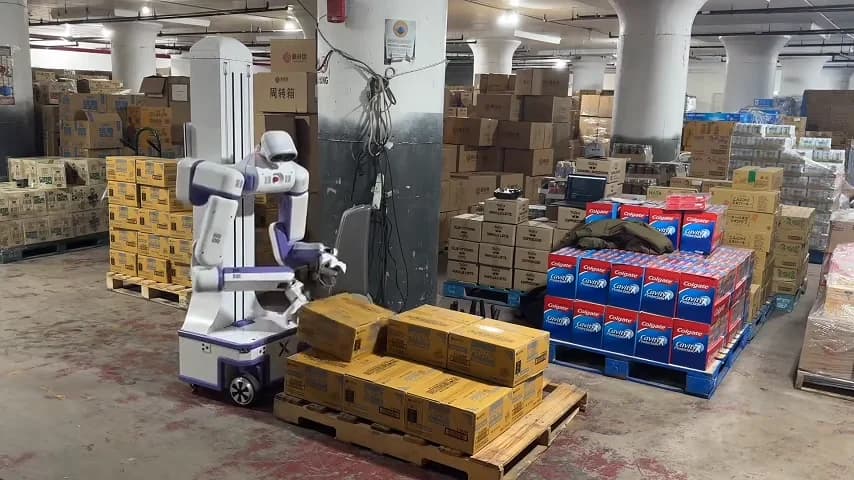 A white and purple Reflex Robotics humanoid robot on a wheeled base moving cardboard boxes in a warehouse environment.