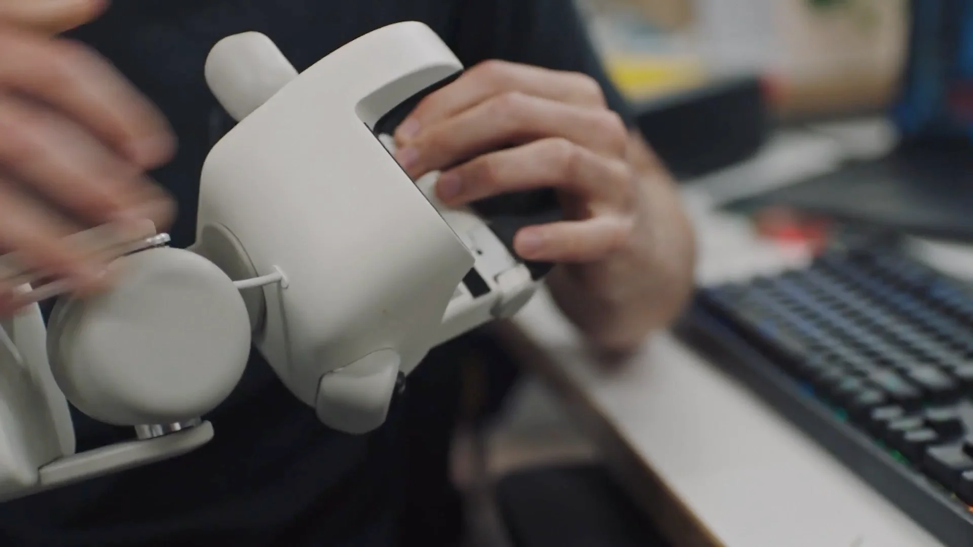 A close-up view of a person's hands holding and adjusting the white, mechanical gripper of the Sunday Robotics device, showing the pincer-like design.