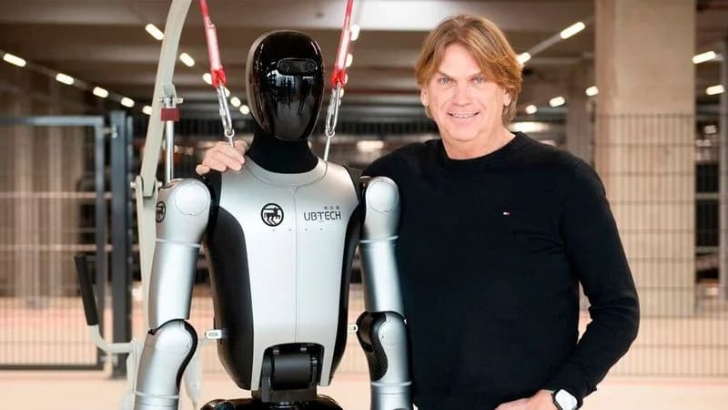Rossmann Logistics Director Hendrik van Duuren stands smiling with his hand on the shoulder of a silver and black UBTECH Walker S2 humanoid robot in a warehouse setting.