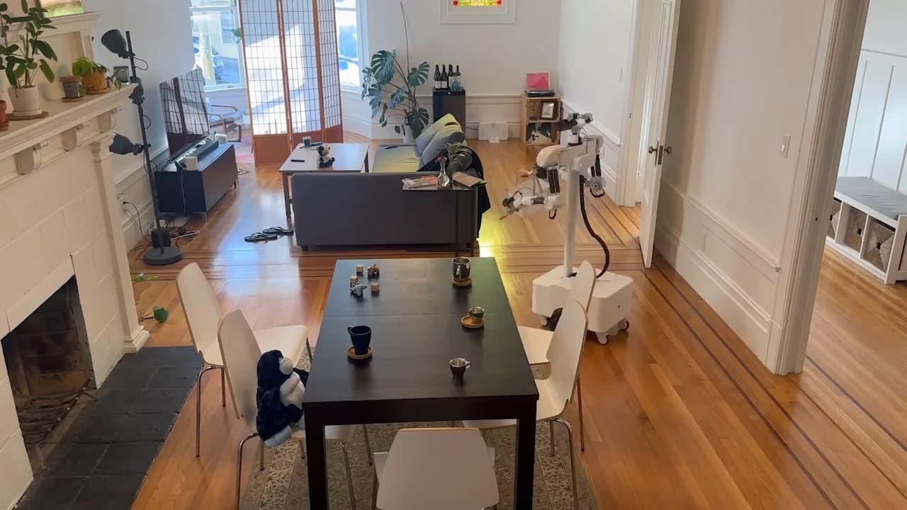 A high-angle view of the Isaac robot tidying a wooden dining table in a modern, open-plan San Francisco apartment.